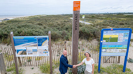Wethouder Michiel Ferwerda en Eveline Buter van Nationaal Park Hollandse Duinen staan bij één van de herkenbare palen die bezoekers duidelijk maken dat ze zich in een nationaal park bevinden.