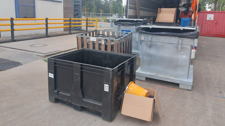 Op de foto zijn meerdere bakken en dozen te zien. Een aantal daarvan staat in de vrachtwagen. Op de achtergrond staat een grijs gebouw.