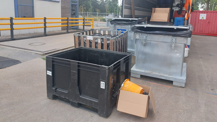 Op de foto zijn meerdere bakken en dozen te zien. Een aantal daarvan staat in de vrachtwagen. Op de achtergrond staat een grijs gebouw.