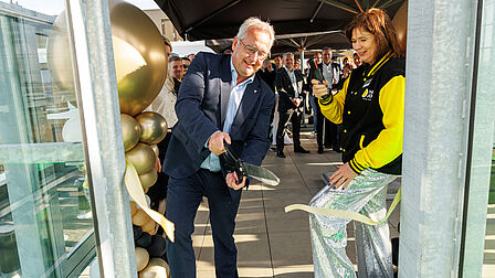 Op de foto knipt een man een lint door met een grote schaar.