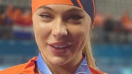 Op de foto laat een vrouw in oranje kleding twee medailles zien. Links op de foto toont zij haar zilveren medaille. Rechts laat zij haar gouden medaille zien.
