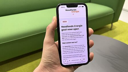 Op de foto is een mobiele telefoon te zien waarop tekst staat geprojecteerd. Op de achtergrond is een grijze tafel, een lichtgroene mat en een felgroene bank te zien.