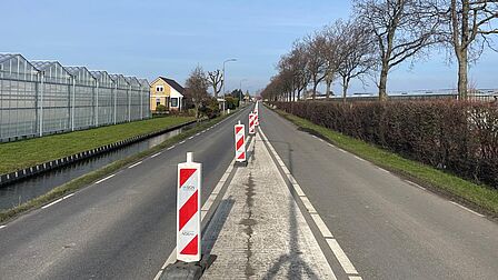 Op de foto is een wegafzetting van rood-witte palen te zien