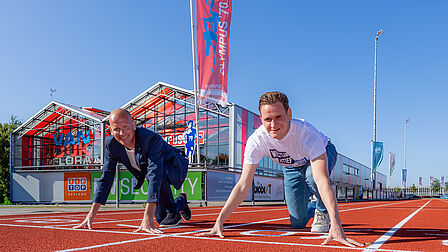 Twee mannen staan op de foto in de starthouding voor een hardloopwedstrijd op een atletiekpiste.