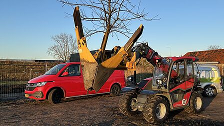 Een gele graafmachine houdt een boom vast.