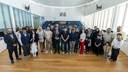 Op de foto poseren meerdere mannen, vrouwen en kinderen op een rij in een raadzaal.