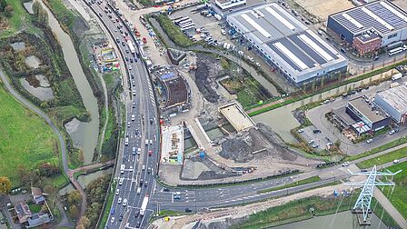 Op de foto zijn meerdere autowegen, bedrijfspanden en een elektriciteitsmast te zien