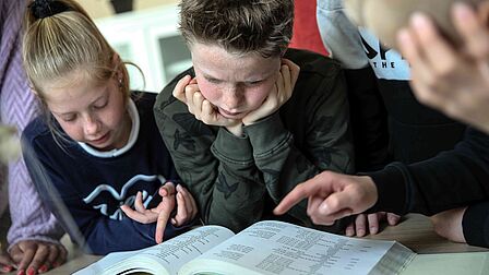 Een meisje en een jongen bekijken een boek met een man.