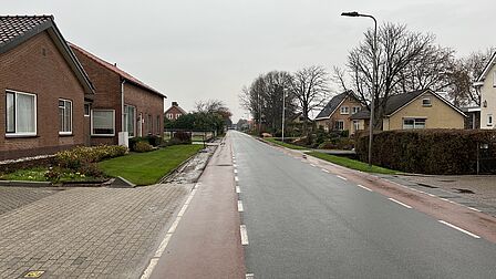 Op de foto si een lange weg te zien met een autoweg en een fietspad erop. Langs de weg ligt een aantal huizen.