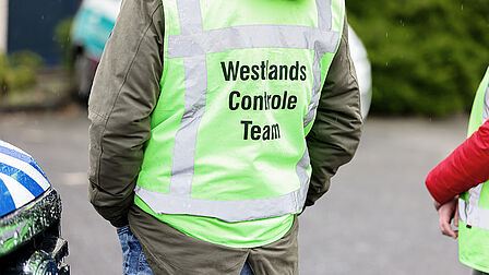 Een man draagt een groen hesje met de tekst 'Westlandse Controle Team' erop